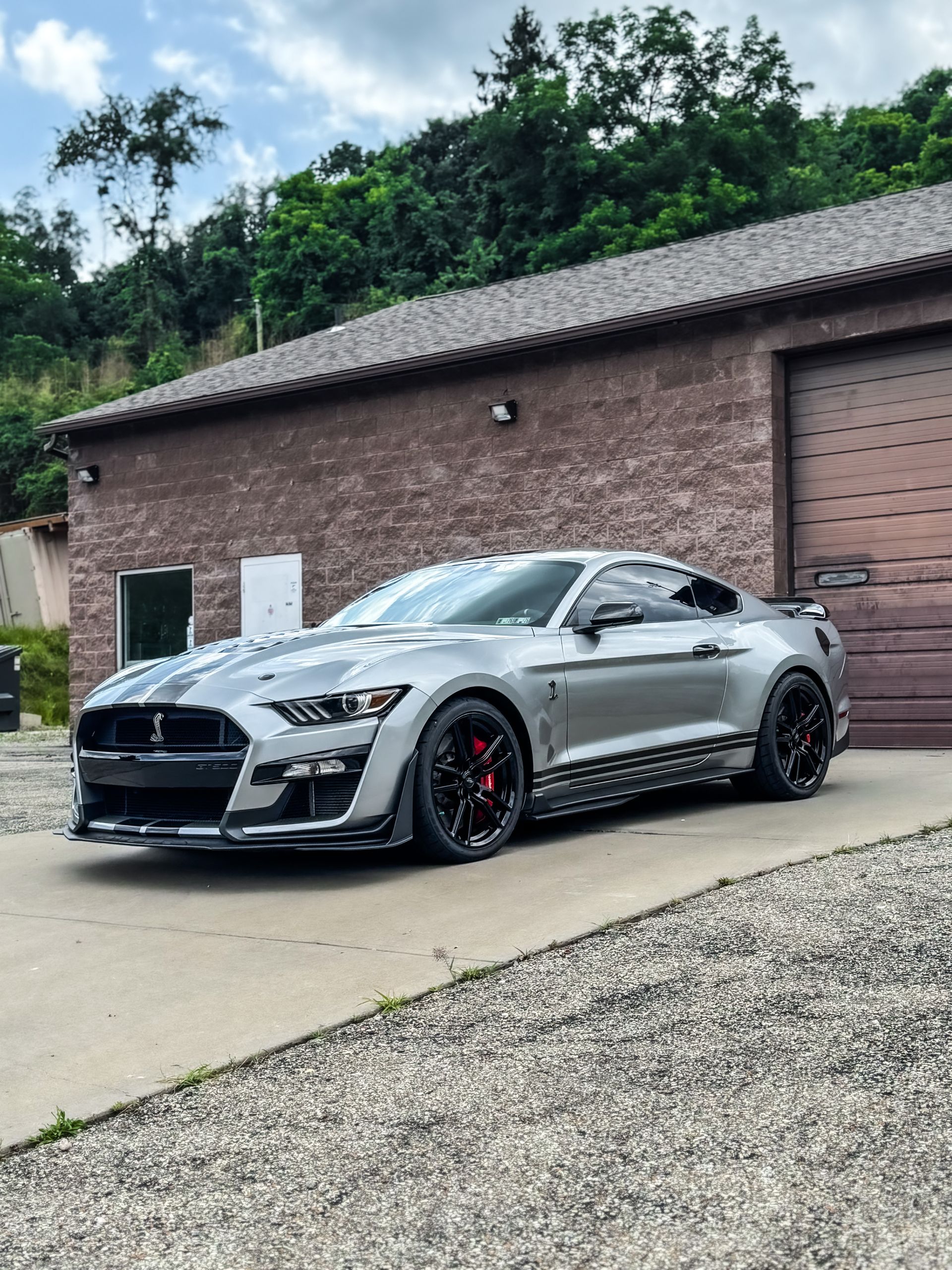 Silver Ford Mustang Shelby GT500 parked outside a brick building with a garage door.