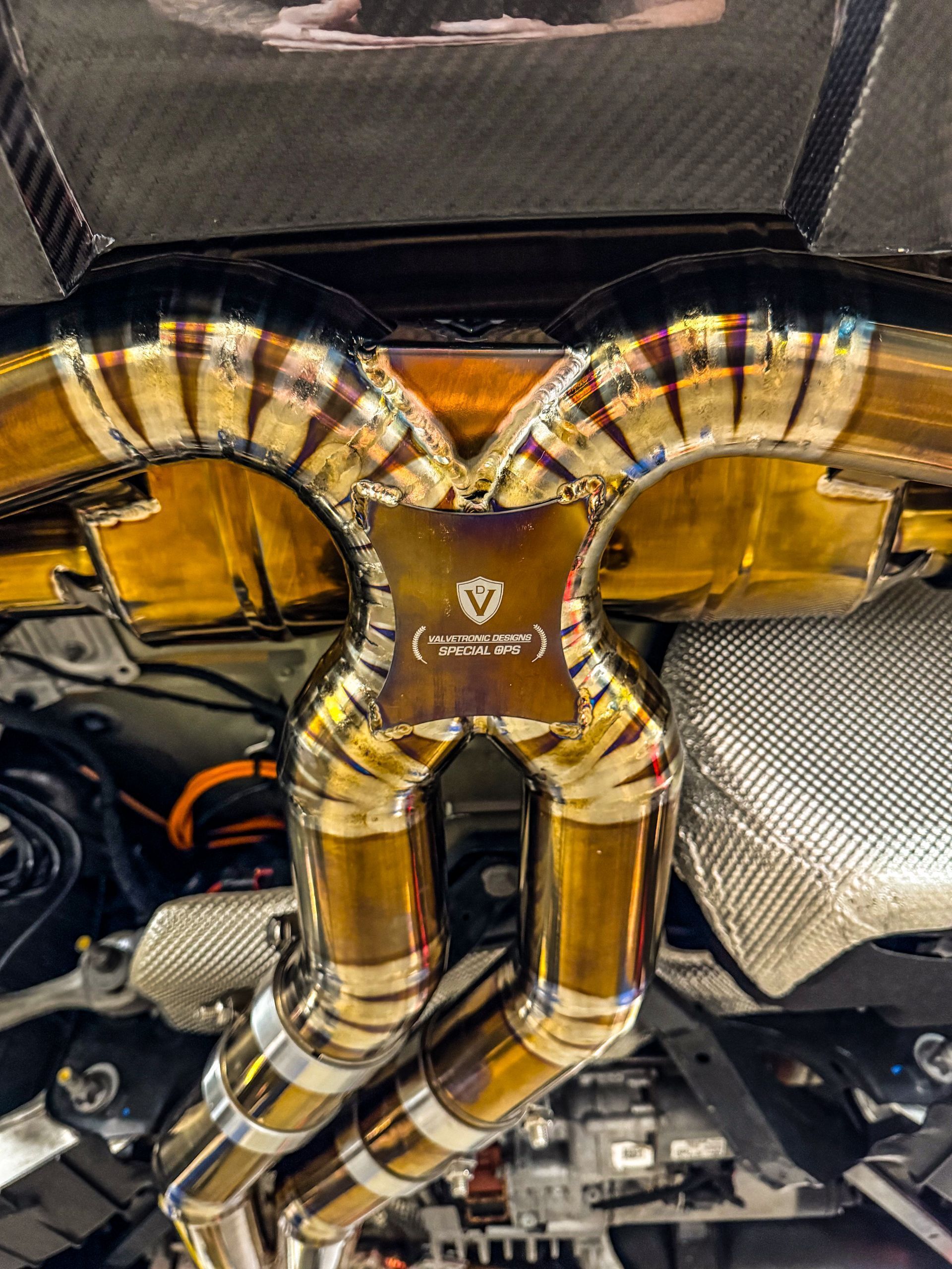 Gold and silver car exhaust system, with visible welds, and a branded central piece.