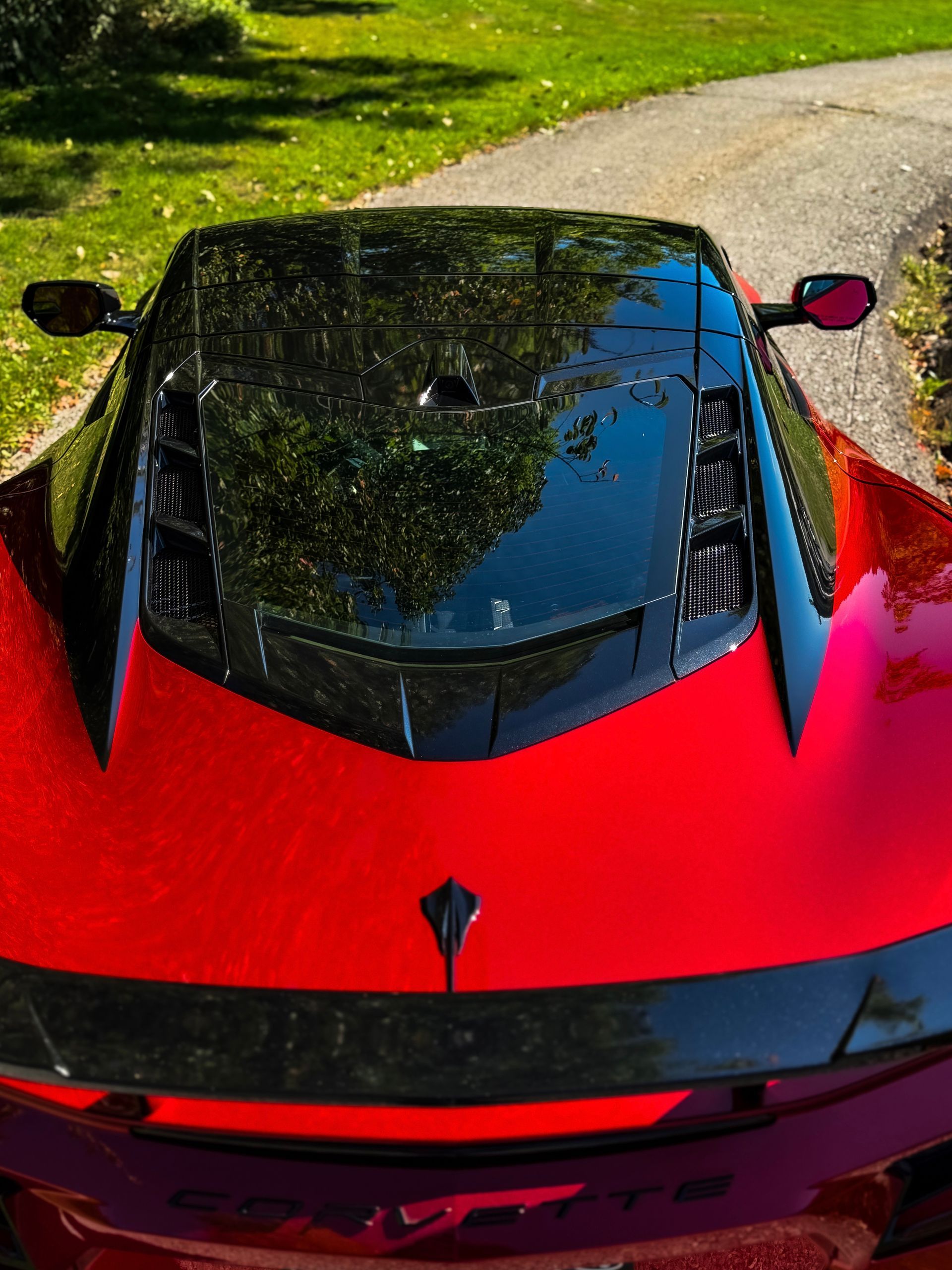 Red Corvette car with black roof, parked on a winding road, sunny.
