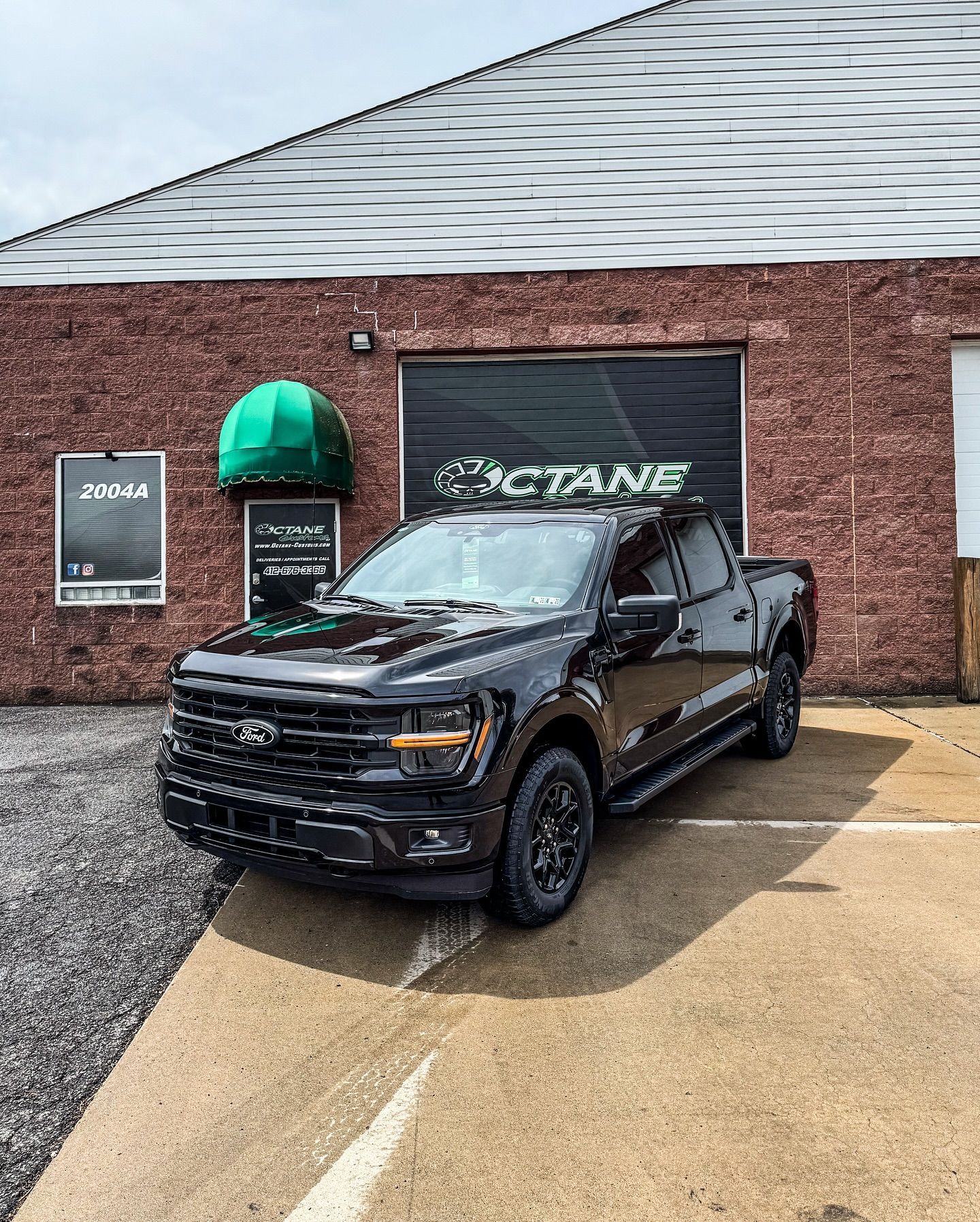 Black Ford pickup truck parked in front of a brick building with a garage door and the word