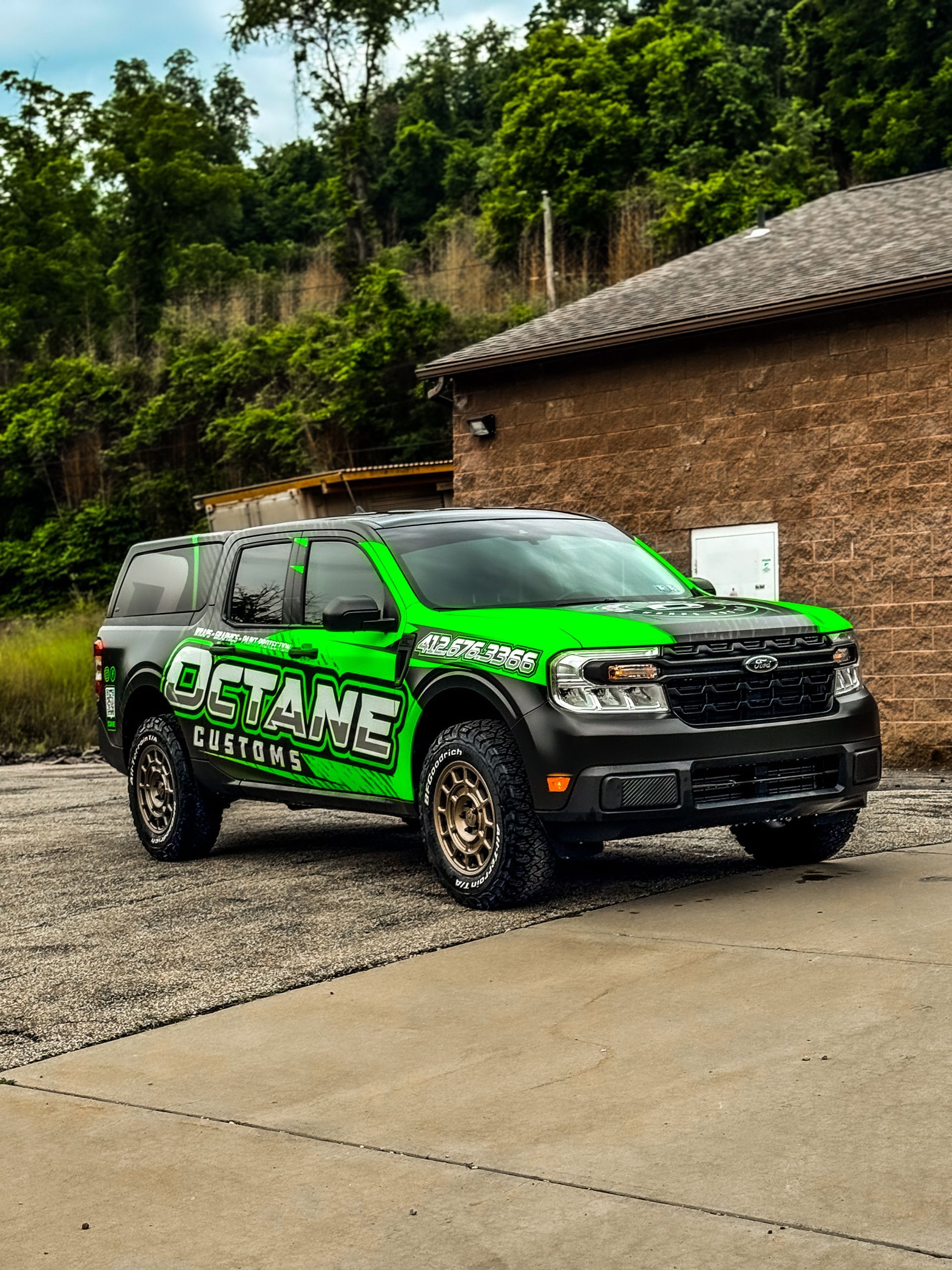 Green and black Octane Customs Ford truck on gravel next to a brick building.