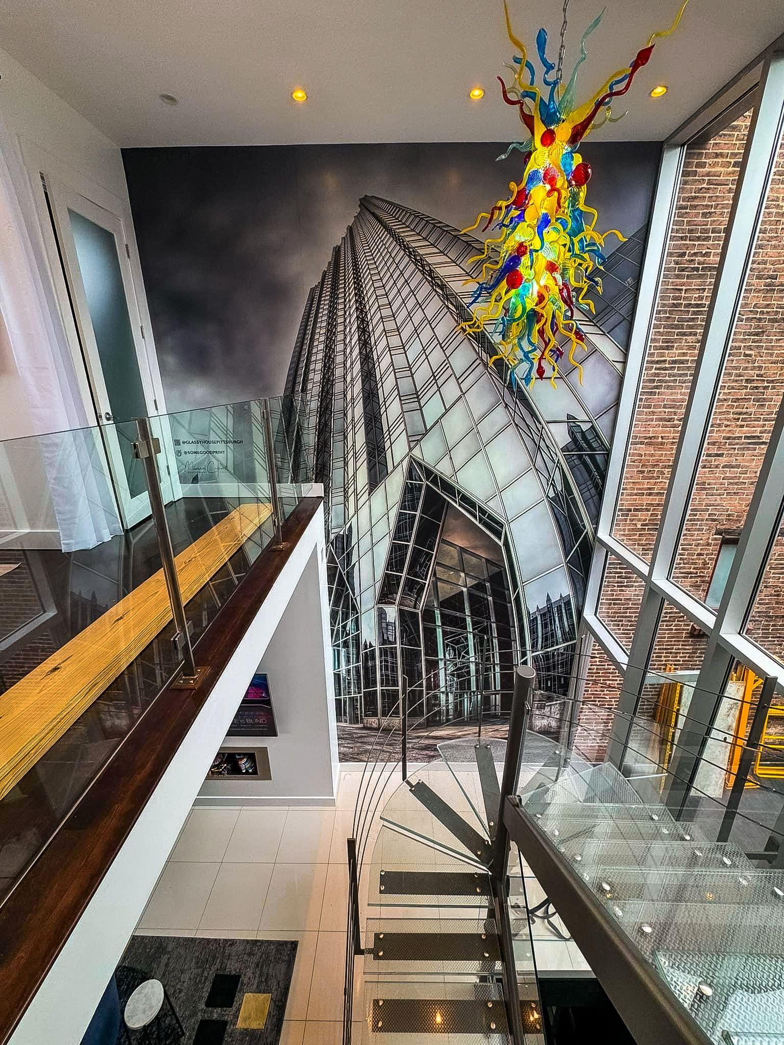 Modern staircase in a glass atrium with a colorful hanging sculpture above.