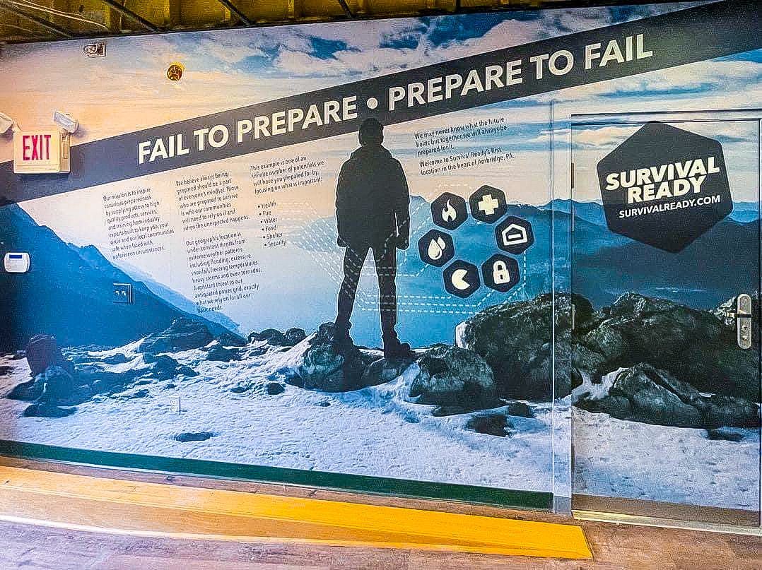 Snowy mountain scene with silhouetted hiker and “Fail to prepare, prepare to fail” survival mural.