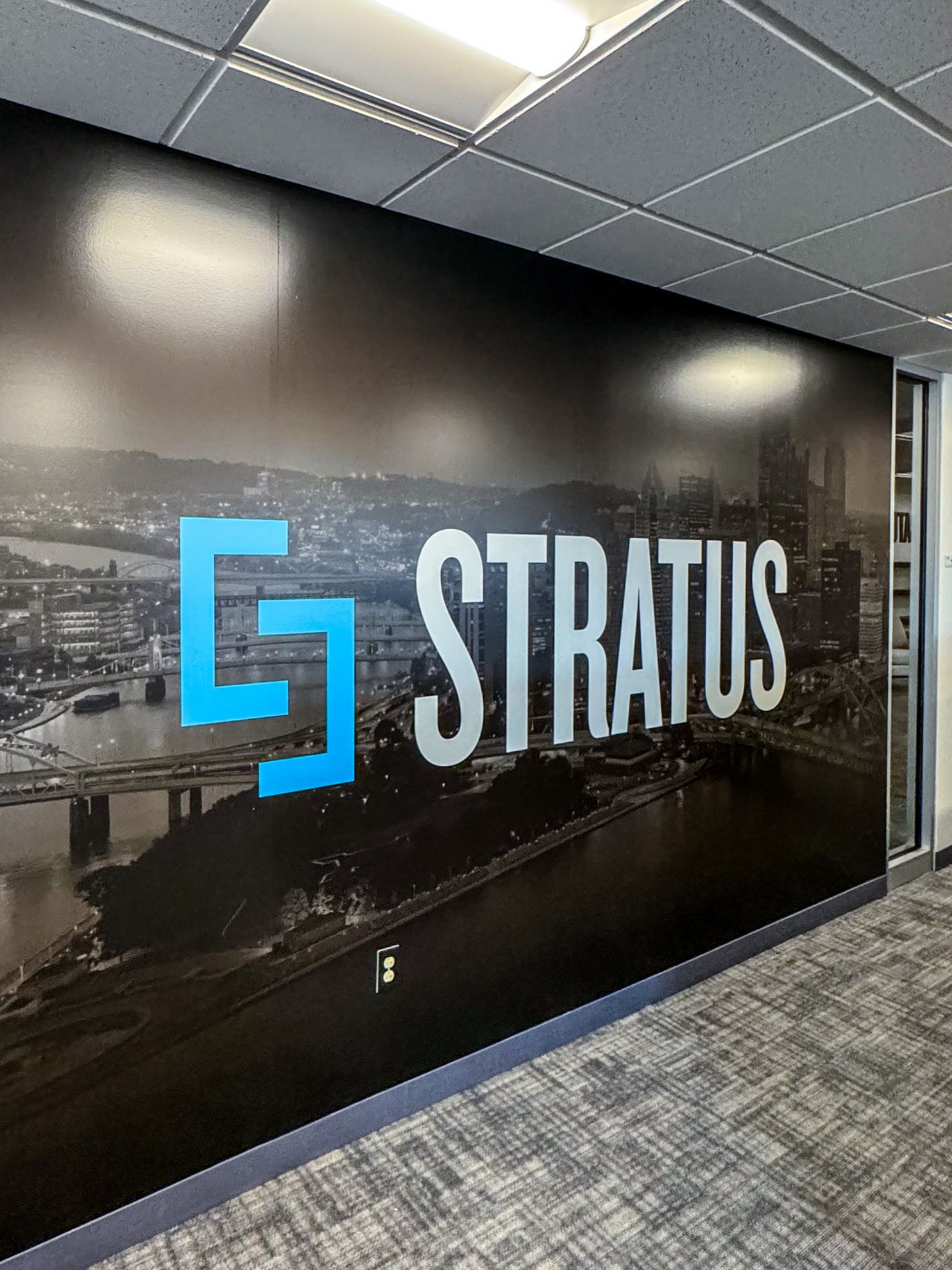 Logo for Stratus in blue and white over a city skyline on a large office wall.