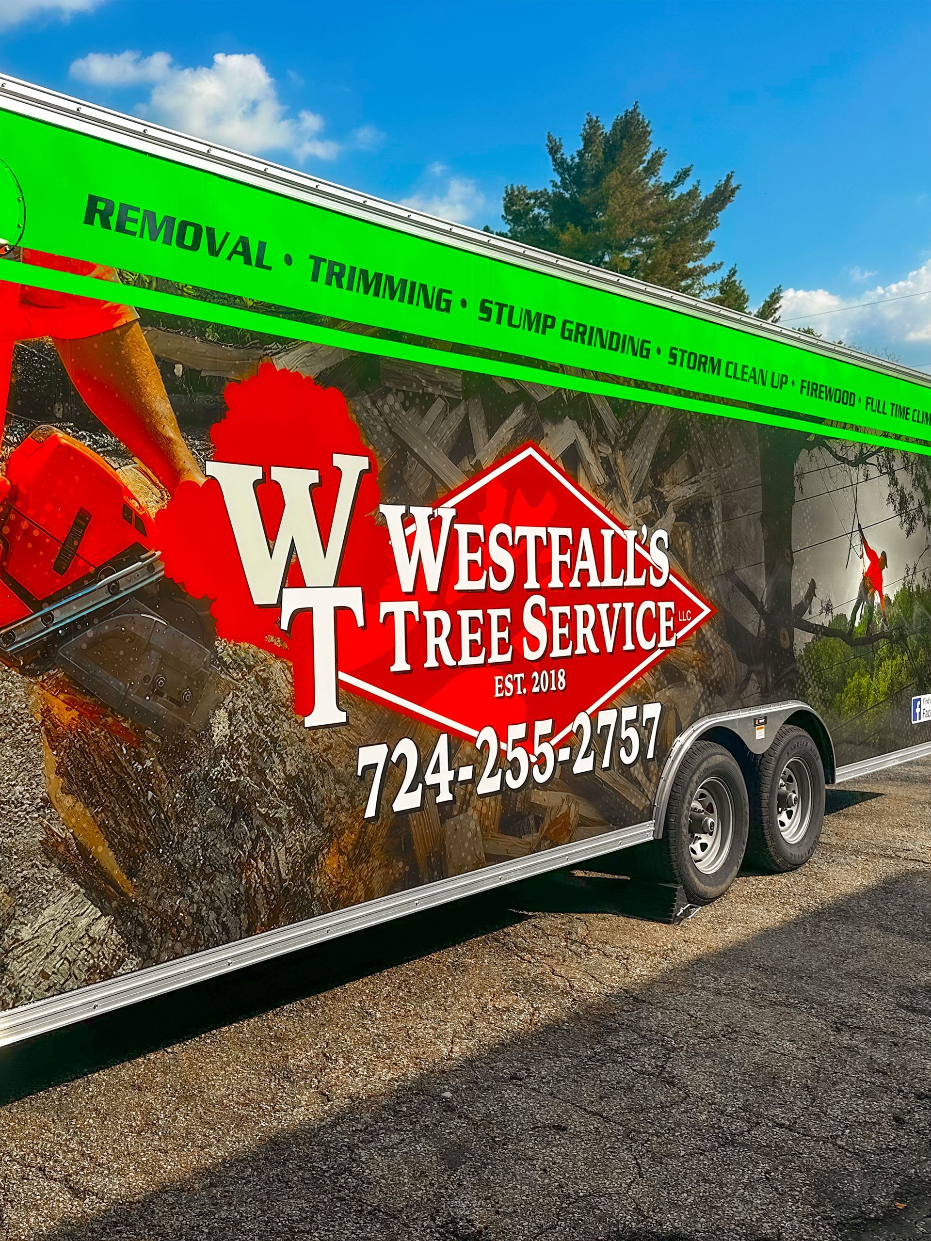 Westfalls Tree Service trailer with logo and contact info; green and red accents, parked outdoors.