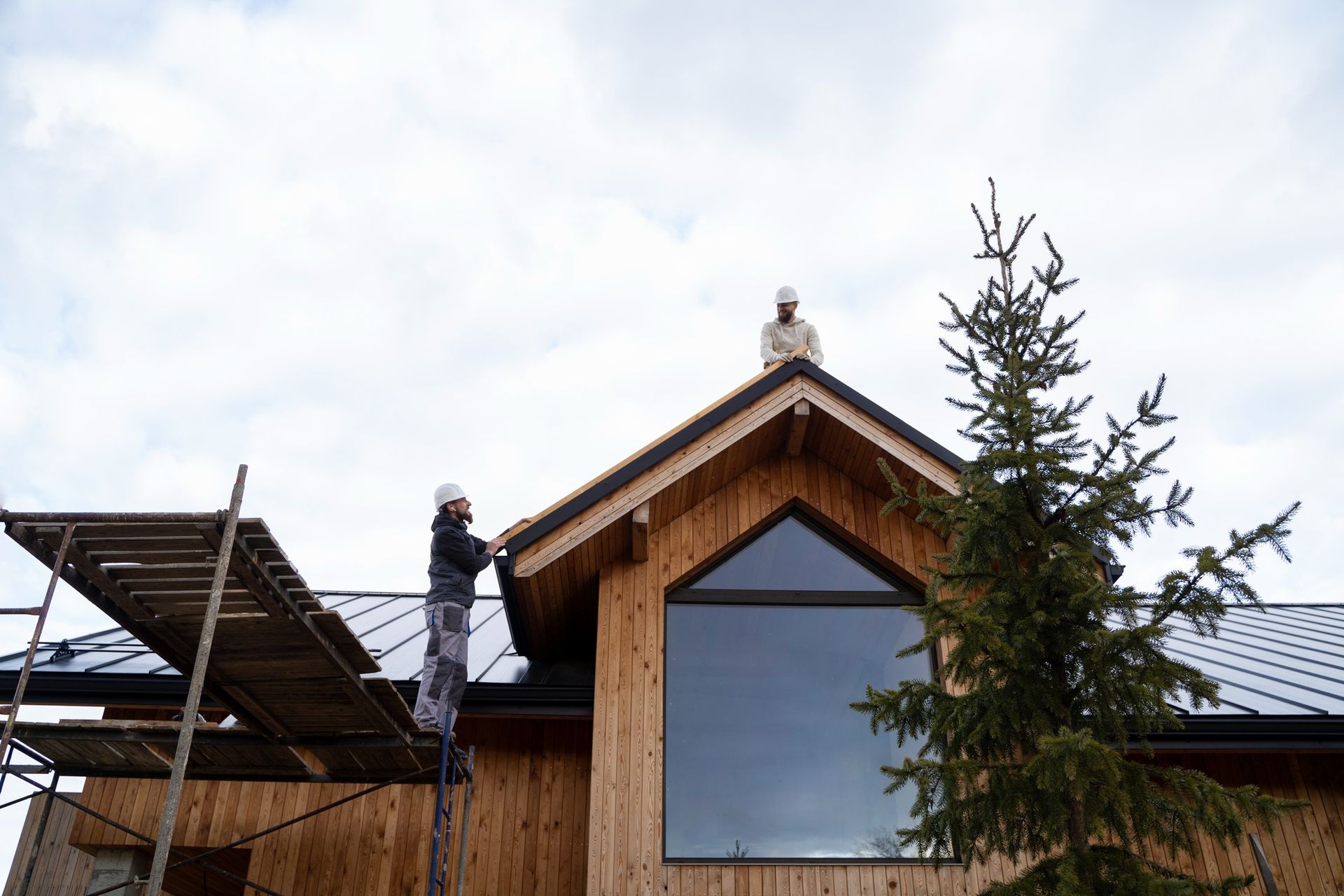 Two men are working on the roof of a wooden house.
