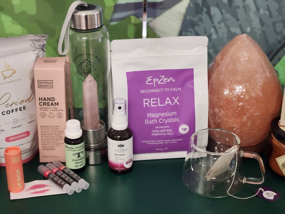 Assortment Of Self-care Items On A Table, Including Crystals, Bath Salts, Lipsticks, Essential Oils, Coffee, And A Glass Water Bottle — Atherton Health Food Centre in Atherton, QLD