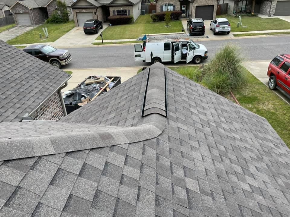A gray shingle roof with a curved edge, viewed from above, with a street and houses in the background.