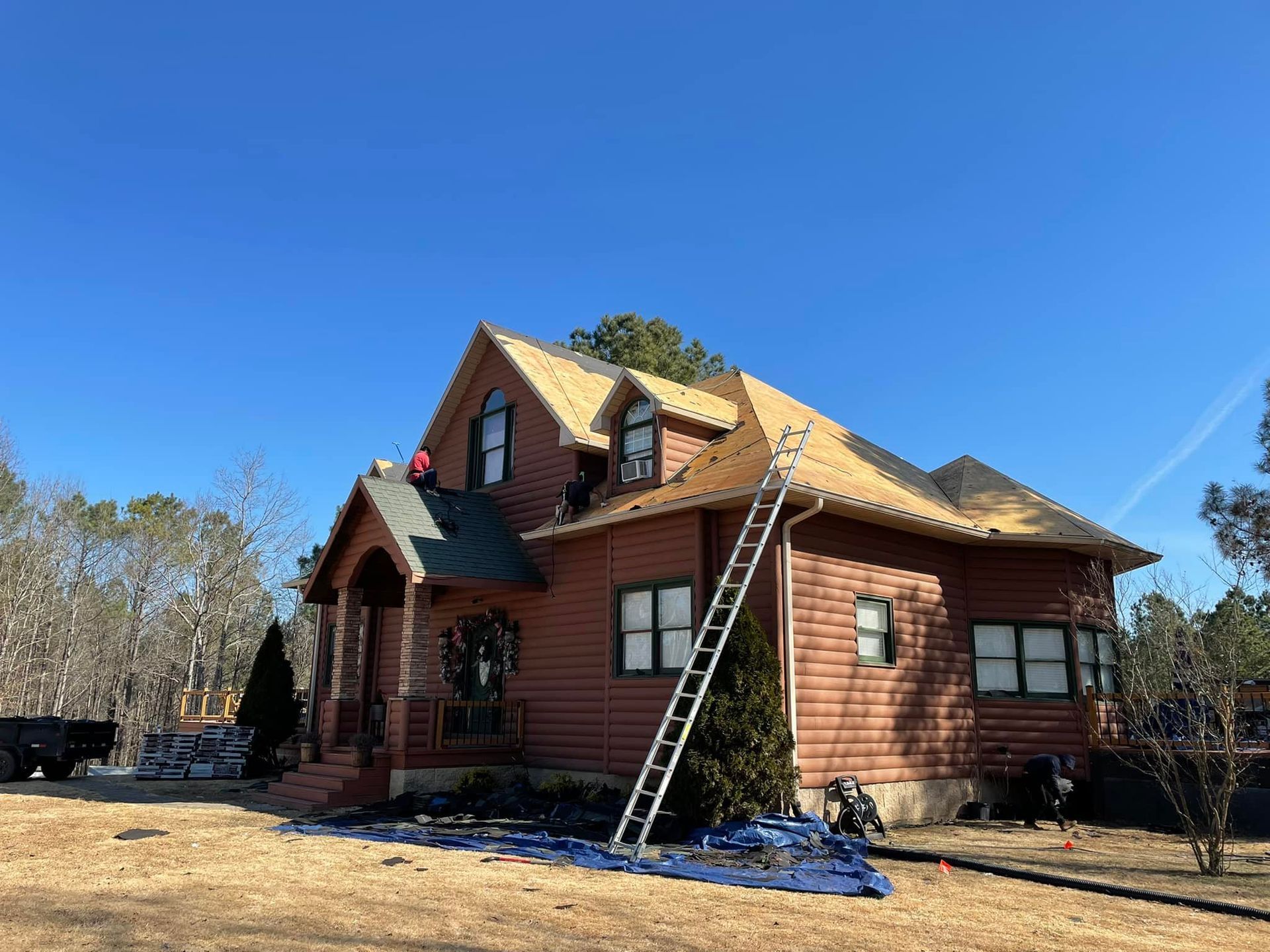 House with roof partially covered in new shingles; ladder propped against the roof, construction in progress.