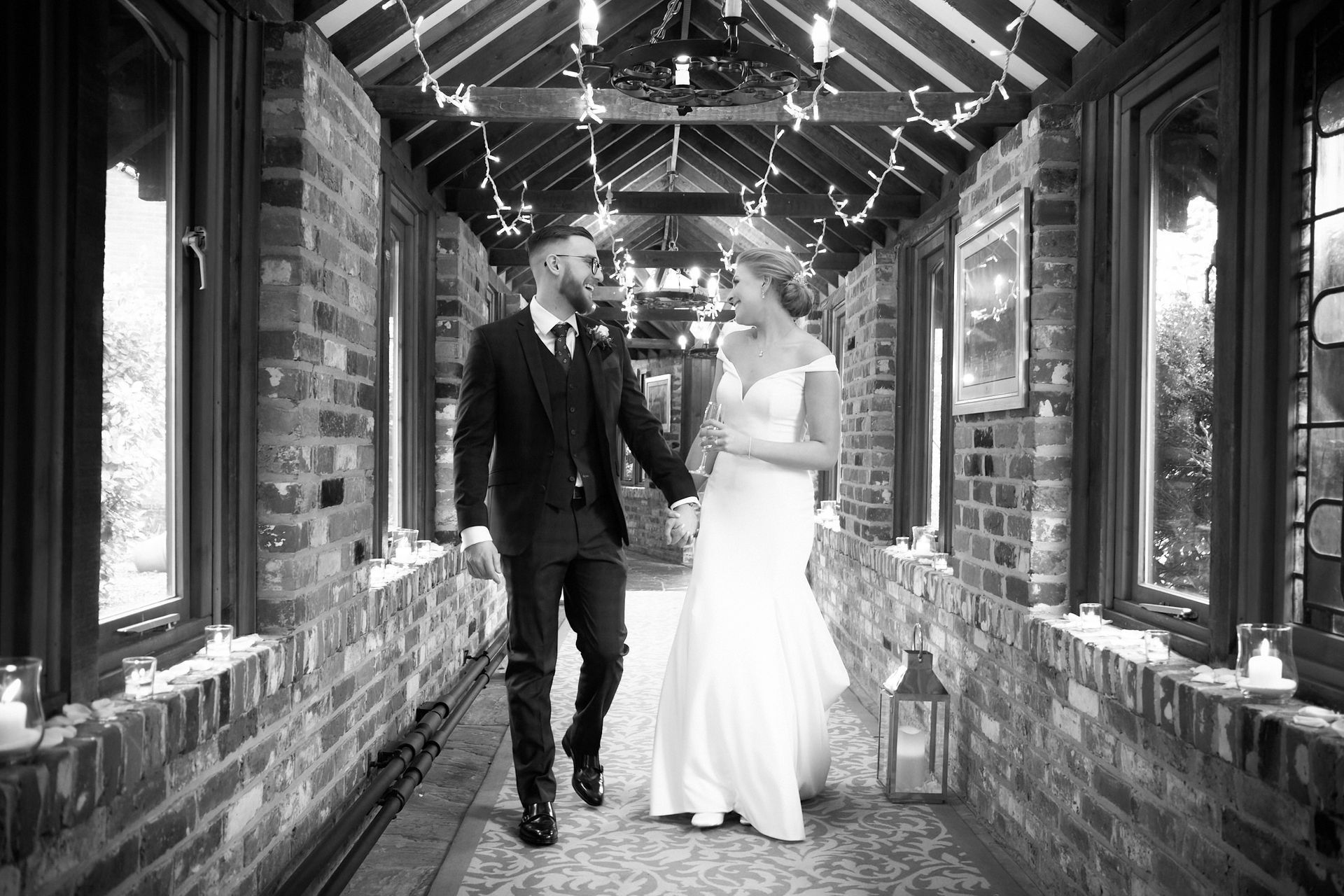 A bride and groom are walking down a hallway holding hands.