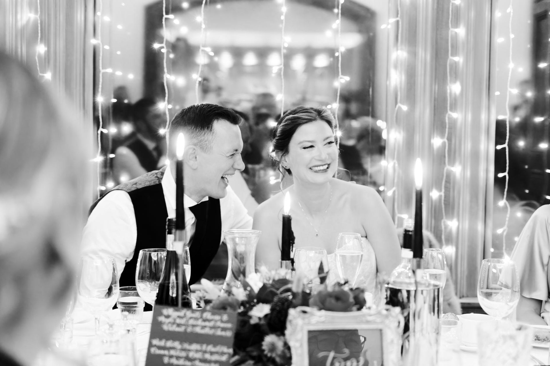 A bride and groom are sitting at a table with candles at a wedding reception.