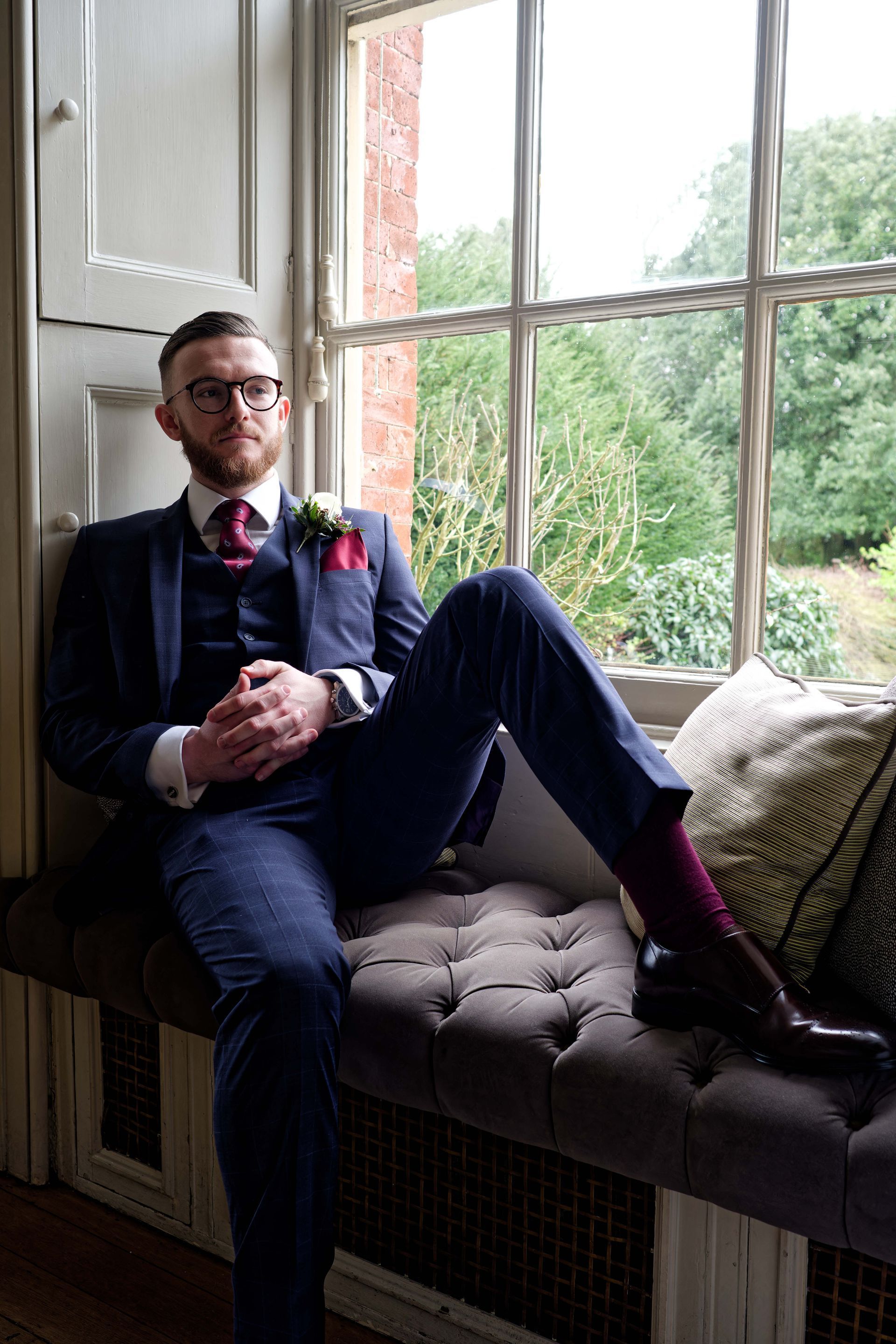 A man in a suit is sitting on a window sill with his legs crossed.