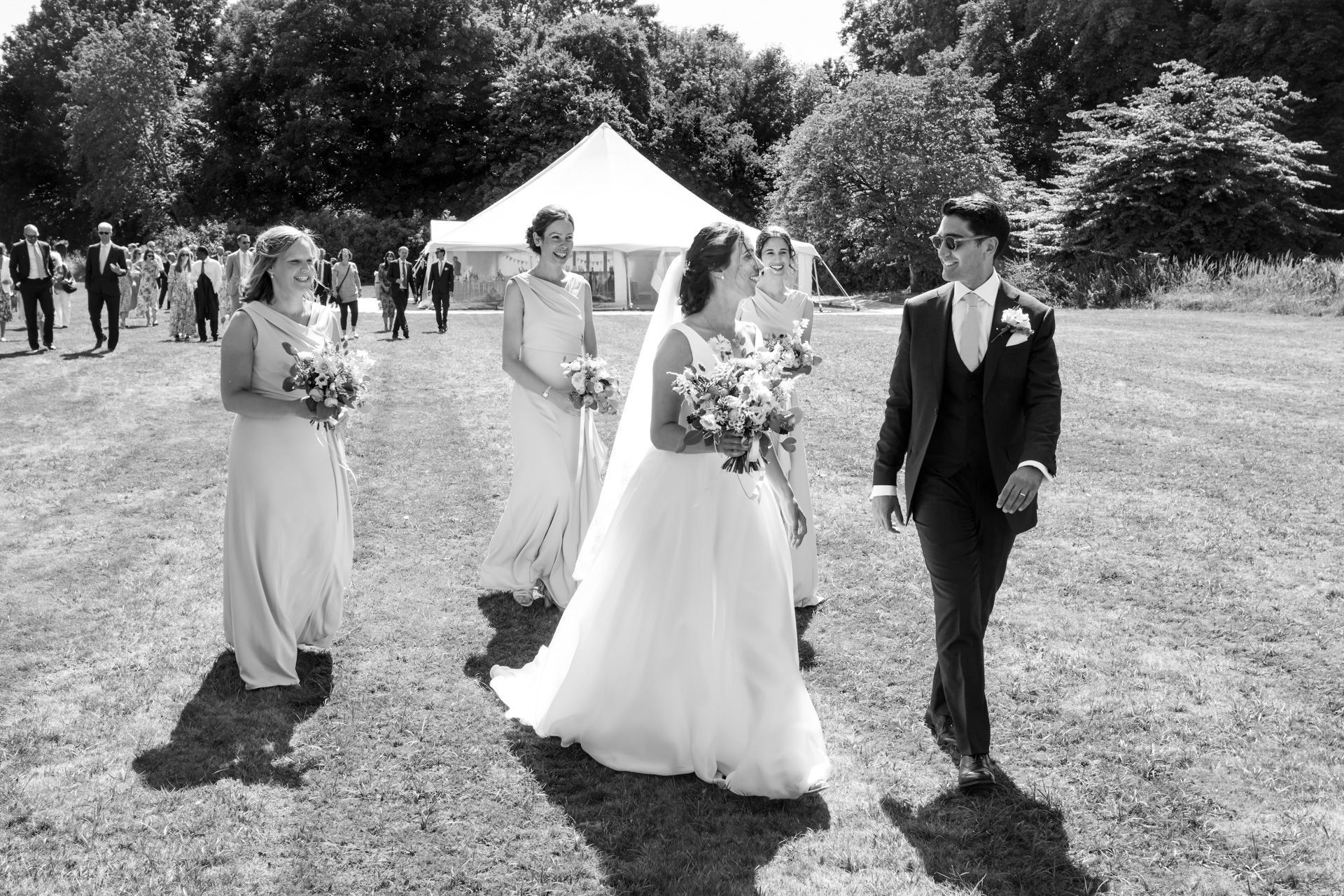 A bride and groom are walking in a field with their wedding party.
