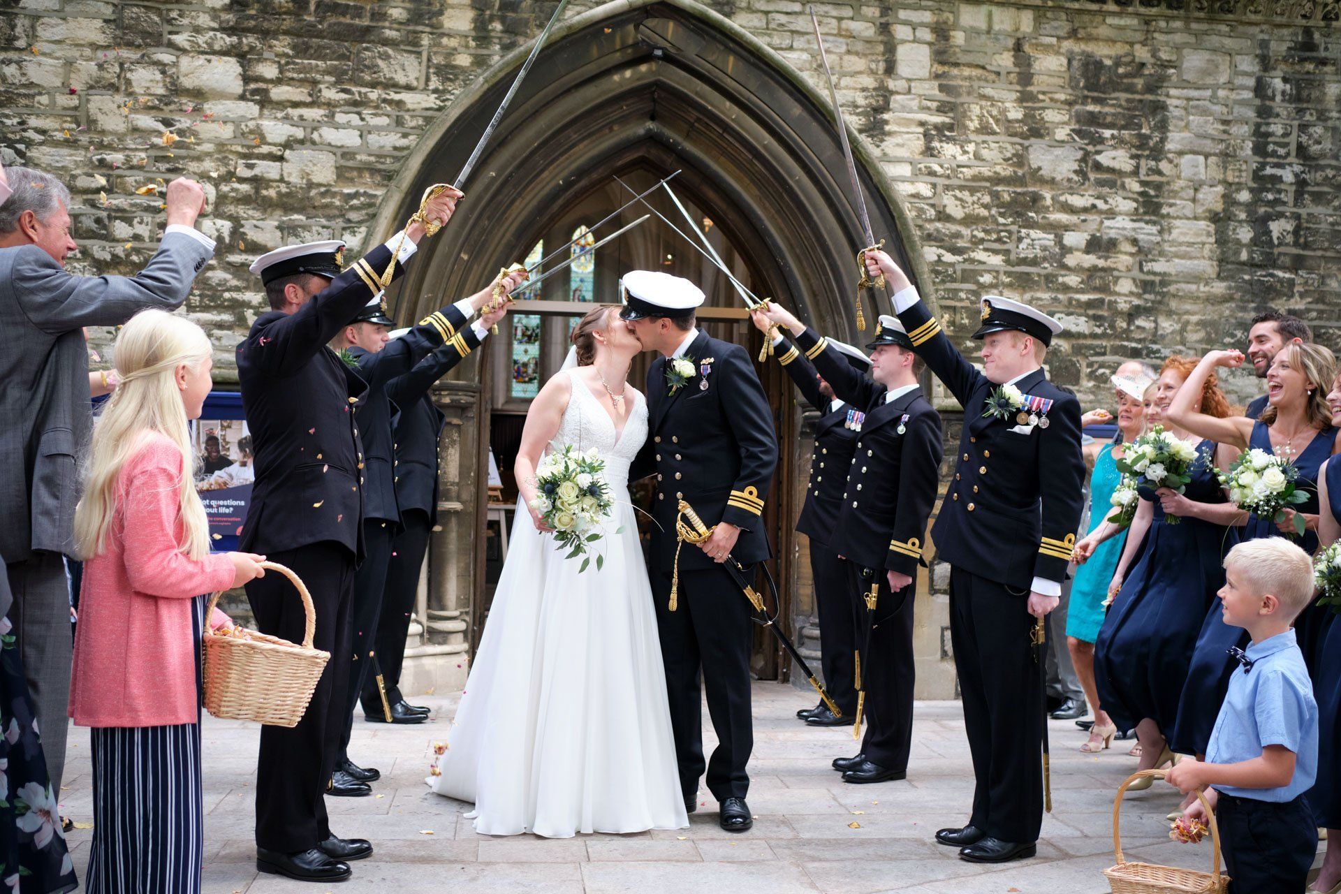 A bride and groom are kissing in front of a church while a group of people throw confetti at them.