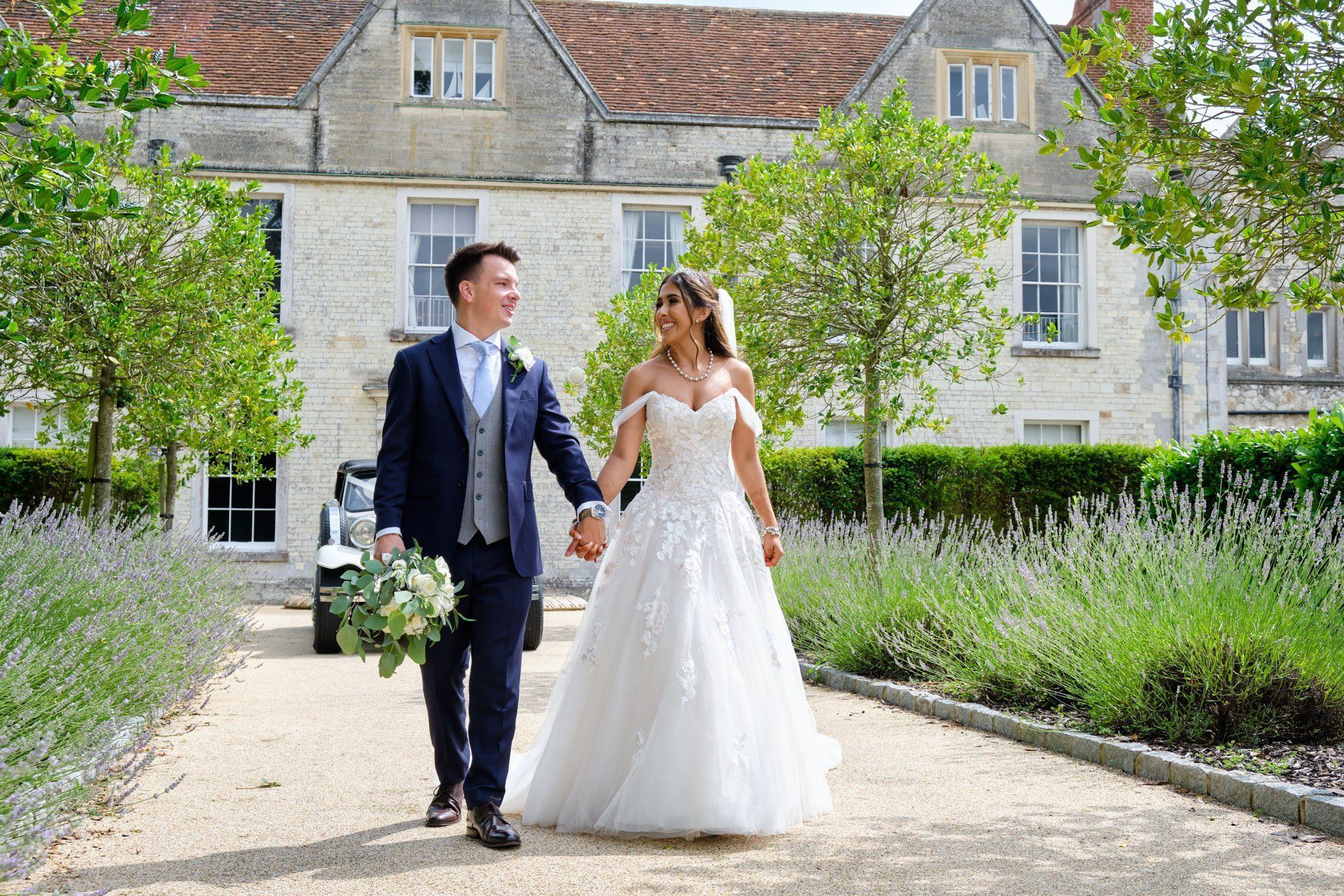 A bride and groom are walking down a path holding hands in front of a large building.