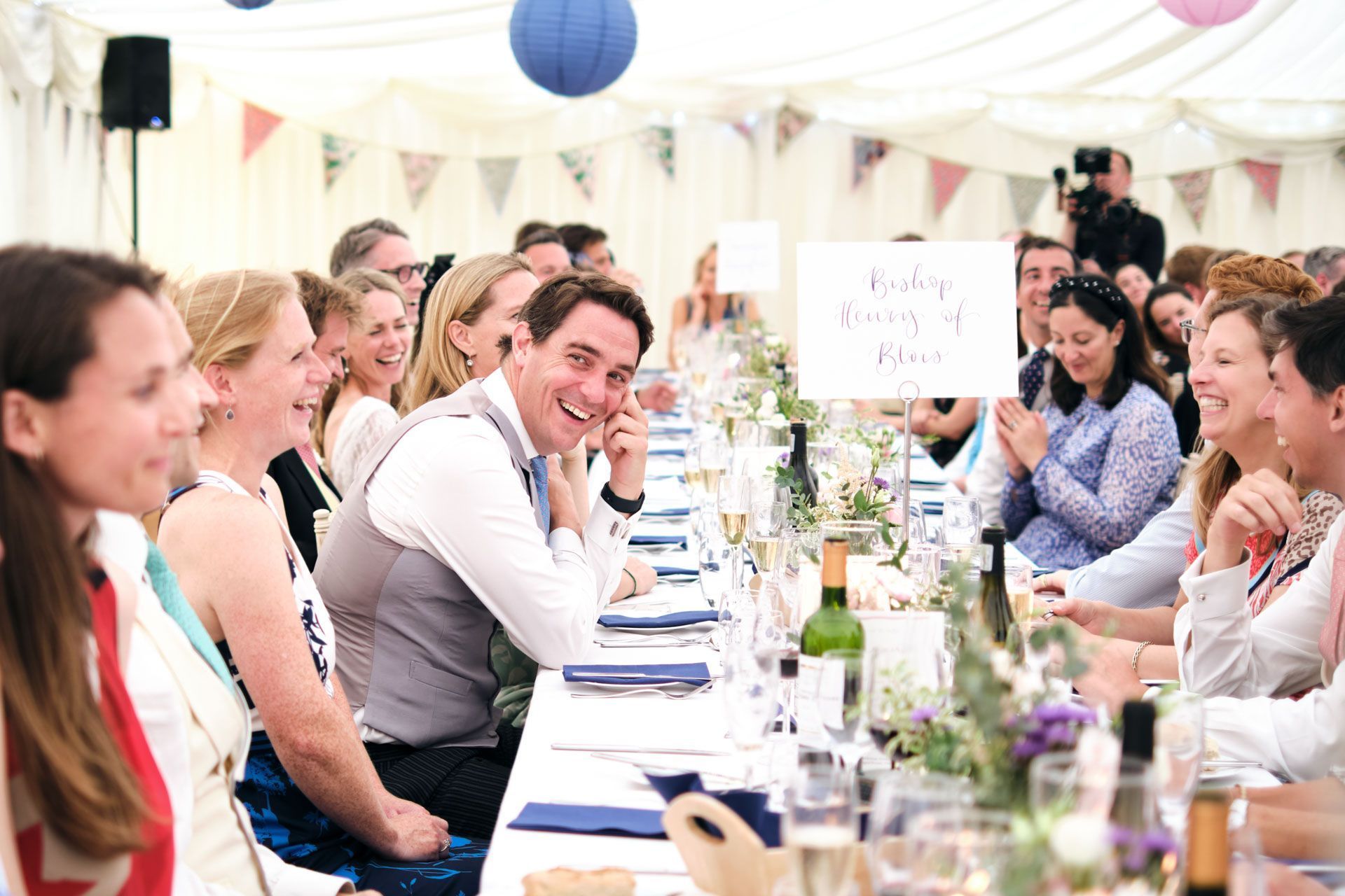 A group of people are sitting at a long table at a wedding reception.