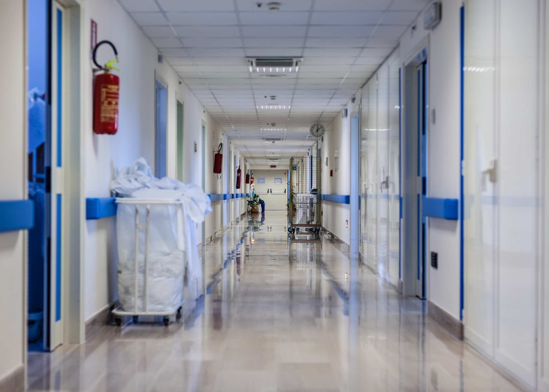 Empty hospital corridor with blue doors, white walls, and cleaning carts on a shiny floor