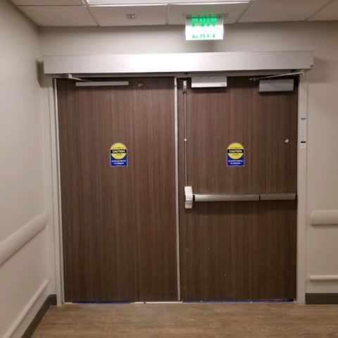 Automatic Doors Installation and Repair - A hospital hallway with a green exit sign above the doors