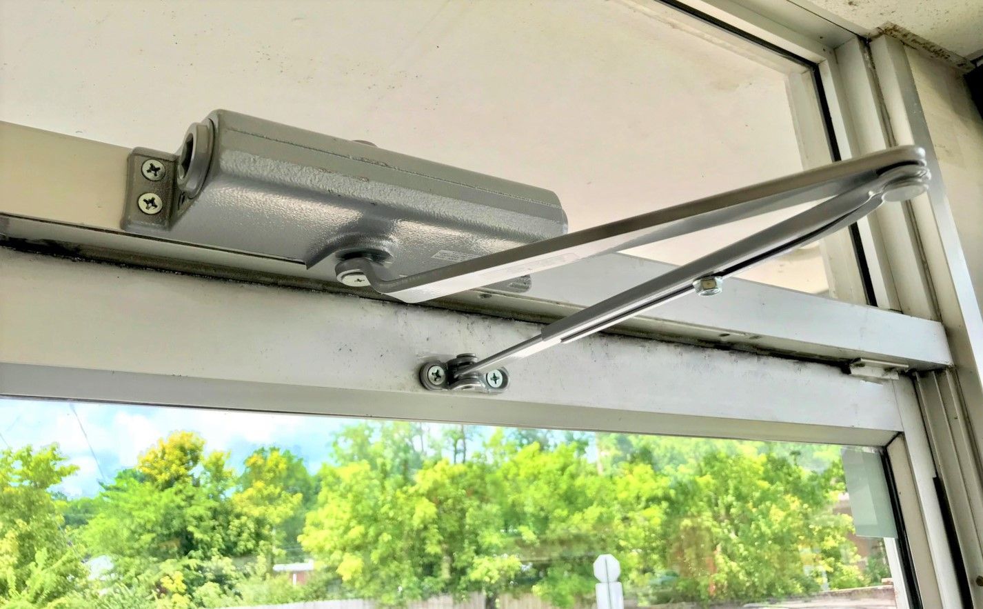 A close up of a door closer on a window.