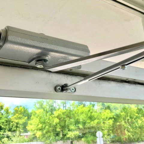 A close up of a door closer on a window with trees in the background