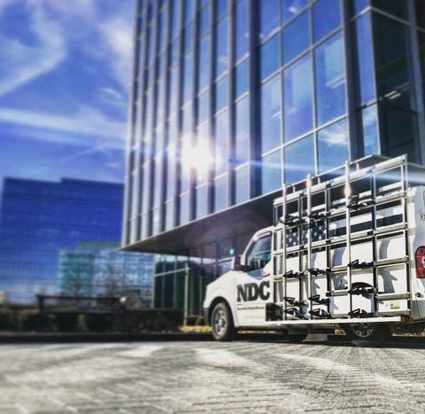 A white ndc truck is parked in front of a building