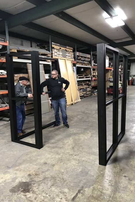 Two men are standing in a warehouse looking at a window frame.