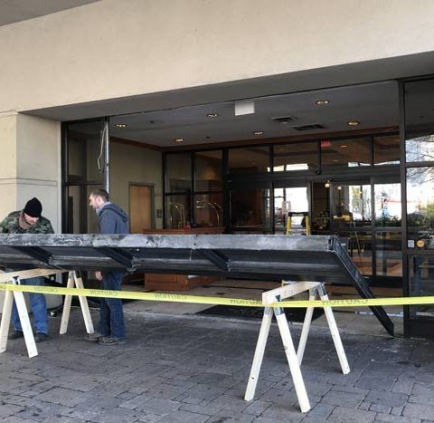 Two men are working on a large piece of metal outside of a building