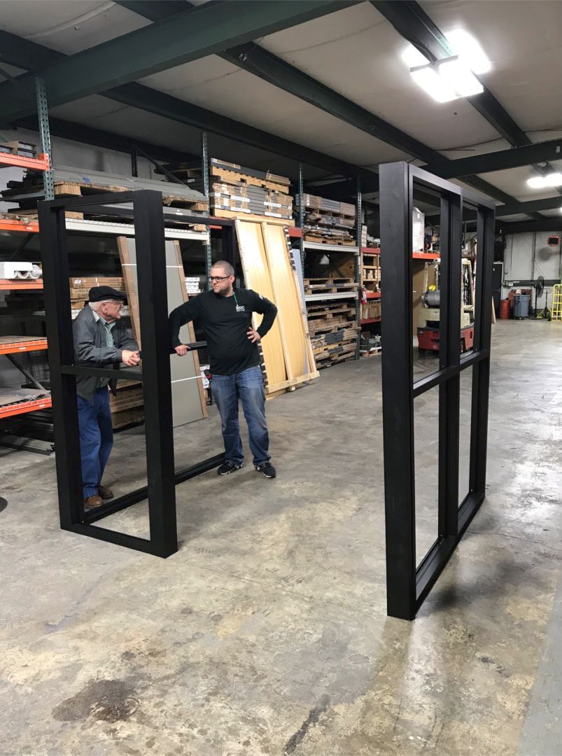 Storefronts & Glass Doors Installation and Repair - Two men are standing in a warehouse looking at a window frame. Storefronts & Glass Doors Installation and Repair - Two men are standing in a warehouse looking at a window frame.