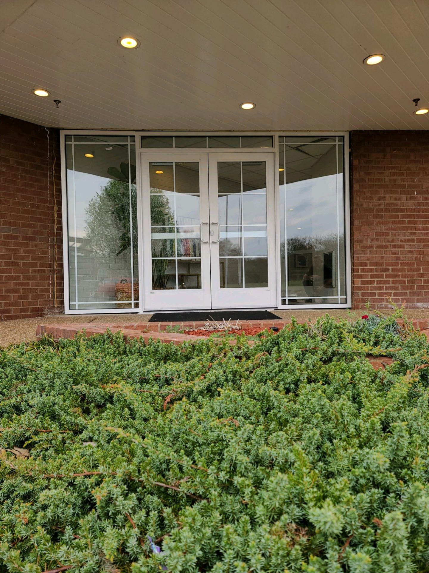 Storefronts & Glass Doors Installation and Repair - A brick building with a white door and a bush in front of it.
