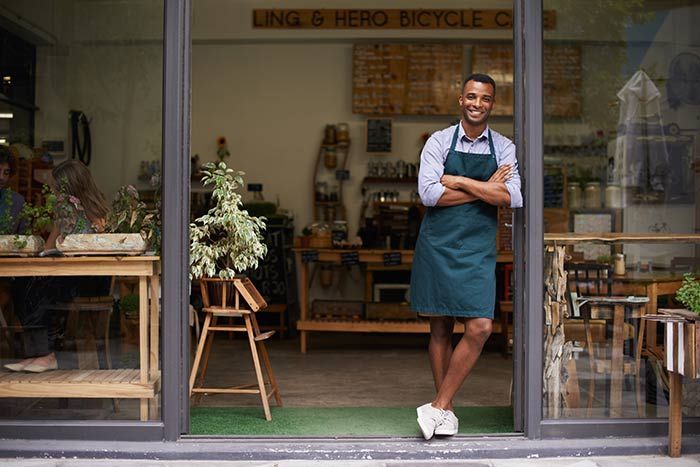 Storefronts & Glass Doors Installation and Repair - A man in an apron is standing in the doorway of a store.