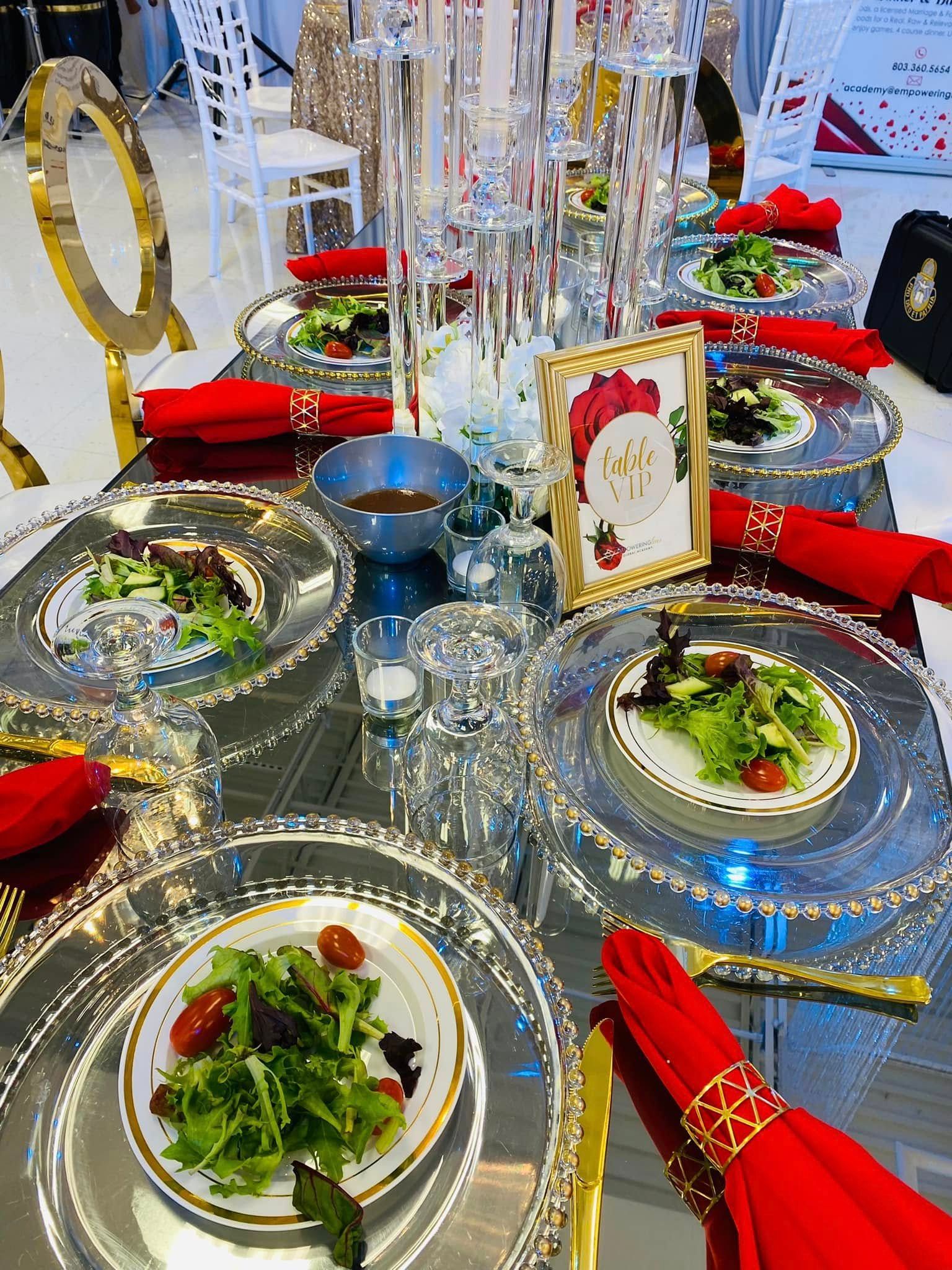 A formal table setting features silver plates topped with small salads, red napkins, and crystal decor on a mirrored table.