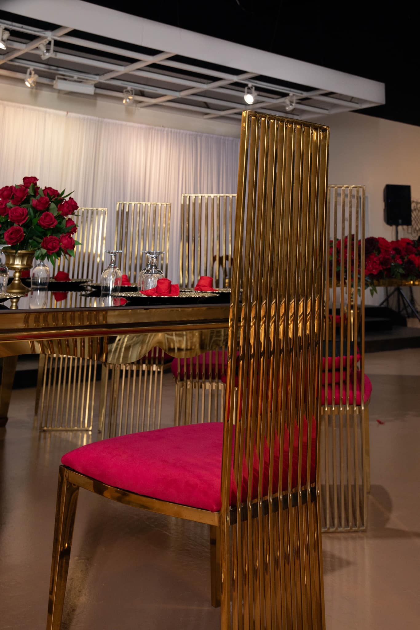 A gold dining chair with a hot pink cushion, positioned near a table decorated with red roses in a well-lit event space.