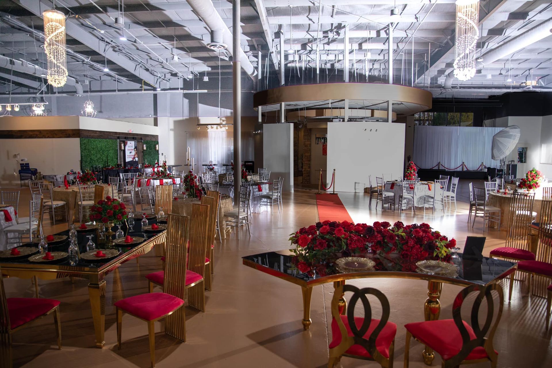 An elegant event hall set for a banquet with tables decorated with red flowers and matching velvet chairs.