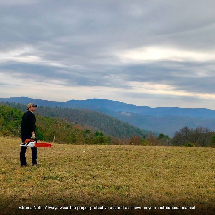 A man standing in a field holding a chainsaw