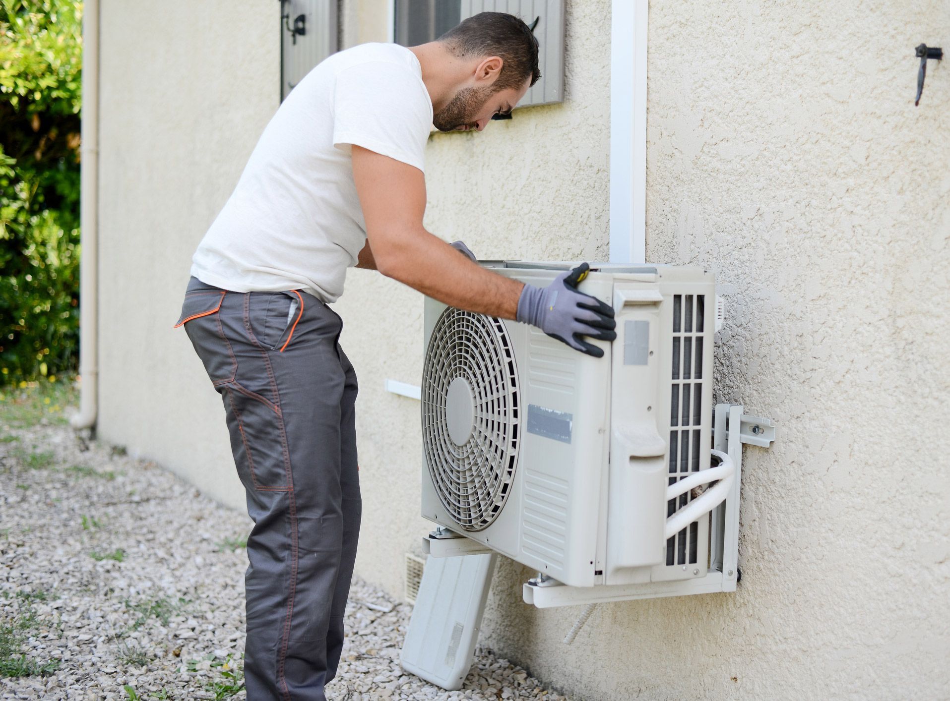 Man installing an air conditioning unit on the exterior wall of a building.