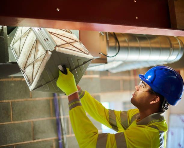 Person installing a white air conditioning unit onto a wall bracket inside a room.