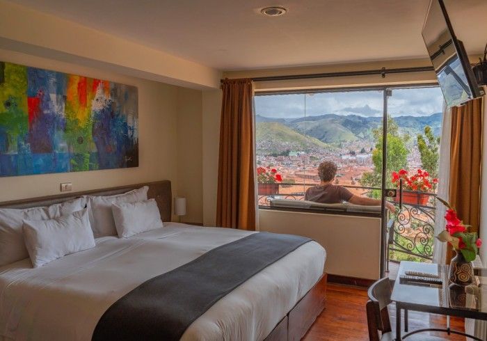 Habitación de hotel con cama, coloridas obras de arte en las paredes y balcón con vistas a las montañas a través de las