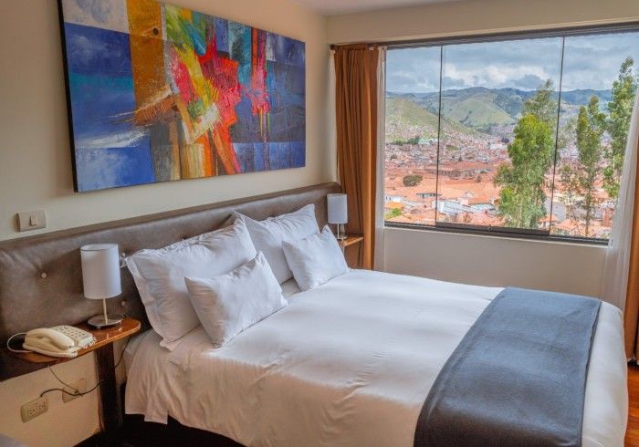 Habitación luminosa con una cama bien hecha, coloridas obras de arte en las paredes y una gran ventana con vistas a