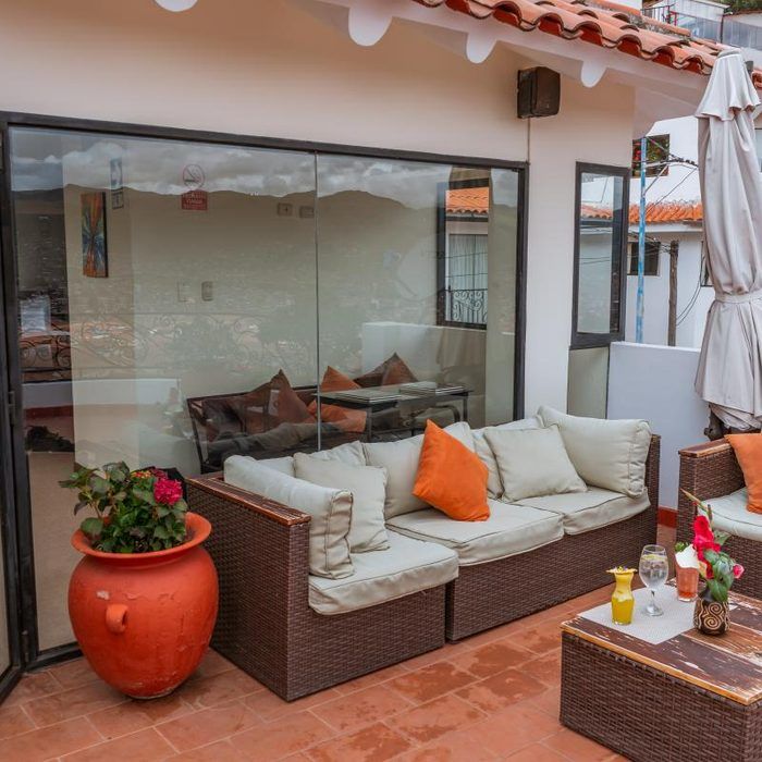 Patio exterior con sofá de mimbre, maceta naranja y mesa de centro junto a una puerta corrediza de cristal.