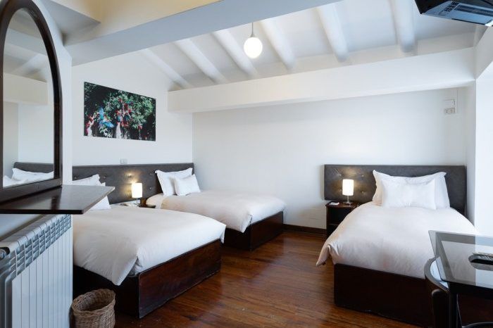 Habitación de hotel luminosa y moderna con dos camas dobles, suelos de madera y lámparas de noche.