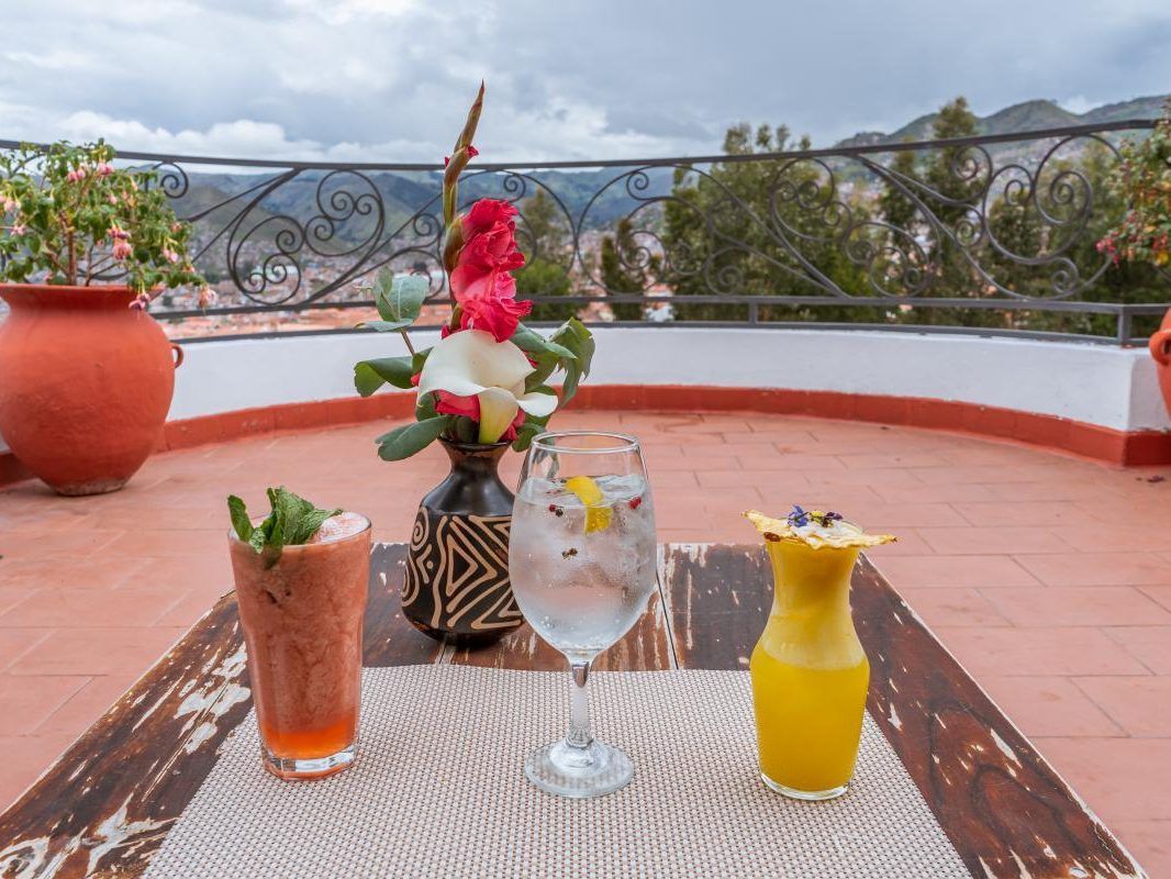 Disfrutar de una bebida en una mesa de terraza con flores y una vista panorámica de la montaña más allá de la barandilla.