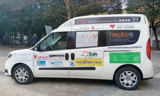 Un furgone bianco con il logo aziendale e la pubblicità è parcheggiato a bordo strada vicino agli alberi.