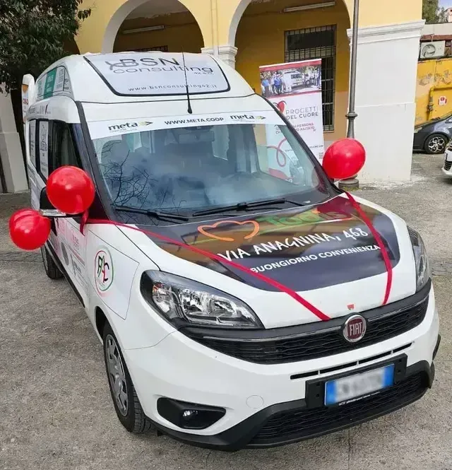 Furgone di servizio Fiat bianco con dettagli rossi e palloncini, parcheggiato davanti a un edificio giallo.