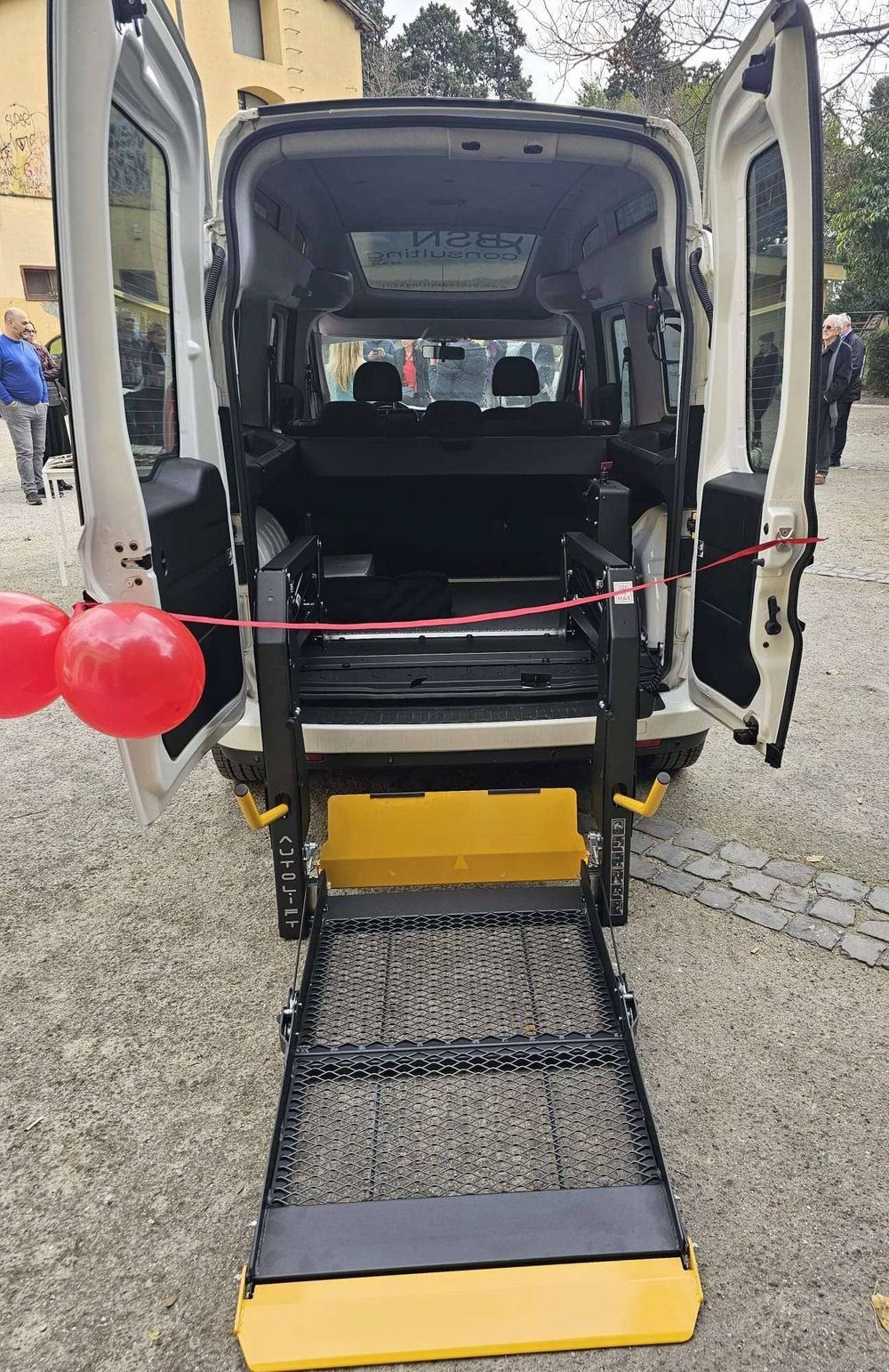 Vista posteriore di un furgone accessibile con rampa per sedia a rotelle estesa e porte aperte su una strada sterrata.