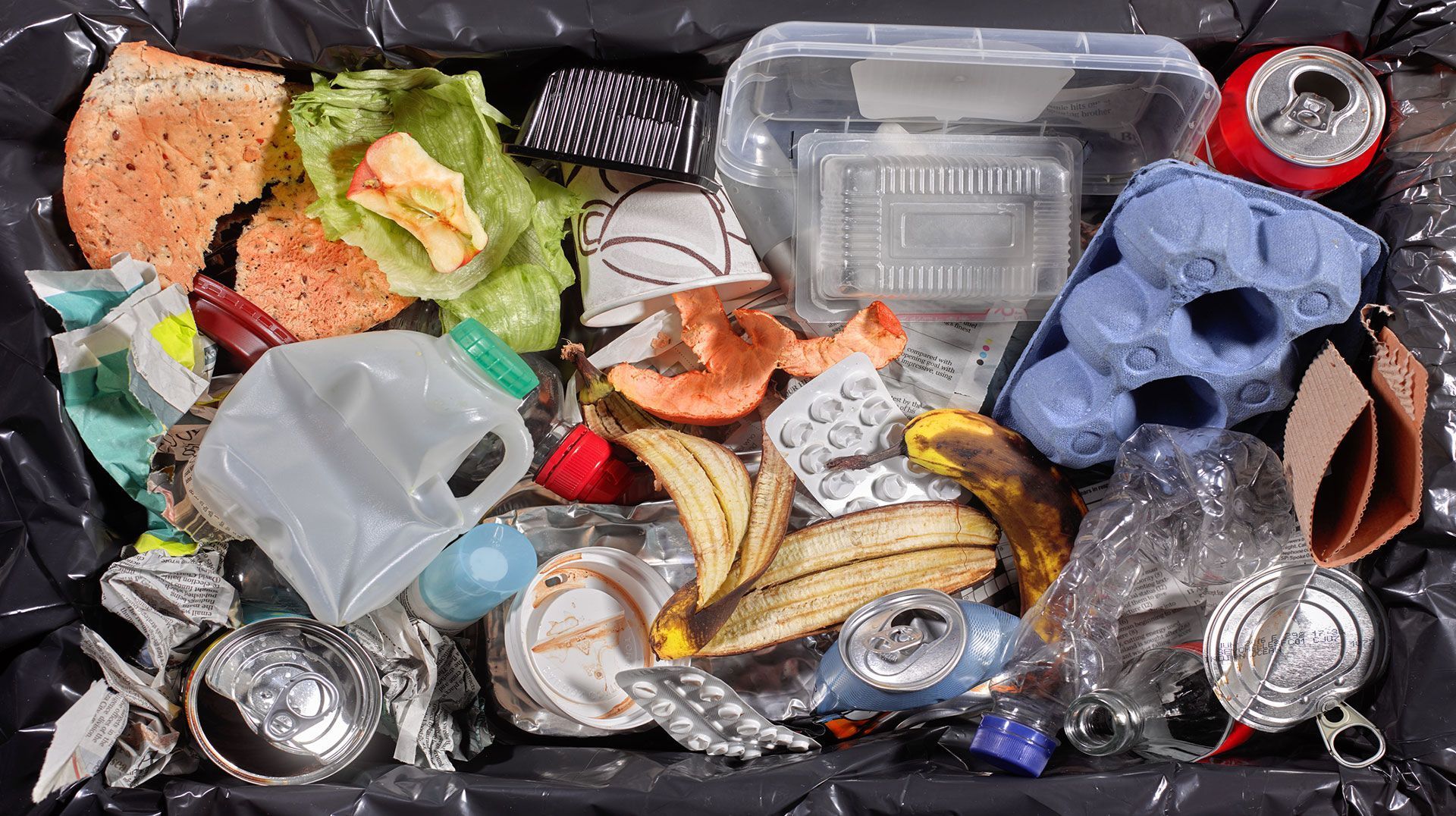 Cestino della spazzatura stracolmo di avanzi di cibo misti, contenitori di plastica, lattine e detriti di imballaggio.