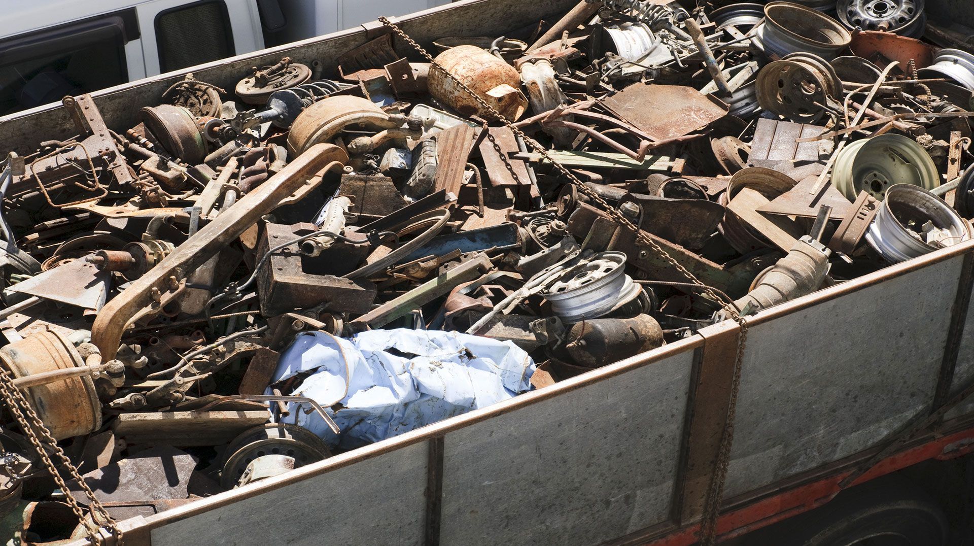 Rimorchio carico di rottami metallici e cianfrusaglie di vario genere, tra cui tubi, ruote e attrezzi.