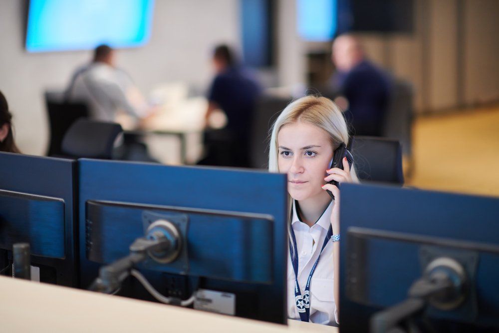 Una donna con le cuffie lavora al computer in un call center, con altri colleghi sullo sfondo.