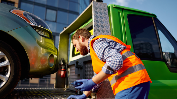 Tow truck driver loading a car onto a flat bed tow truck.