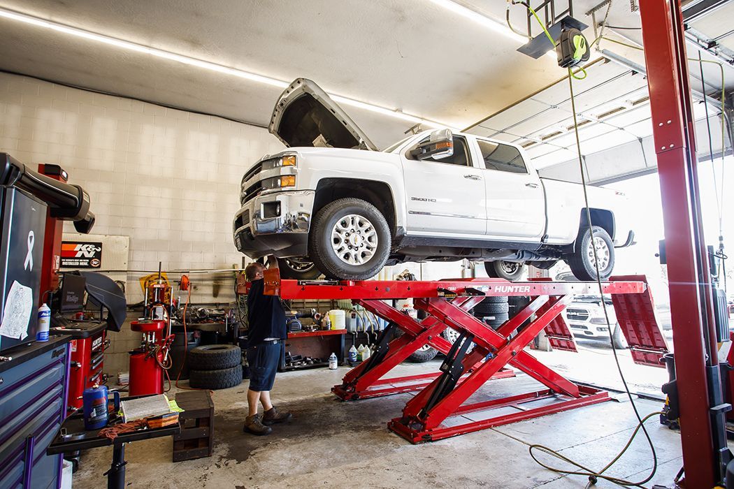 White truck with hood up on red lifts inside of our garage in Centerville, UT | Baker Automotive