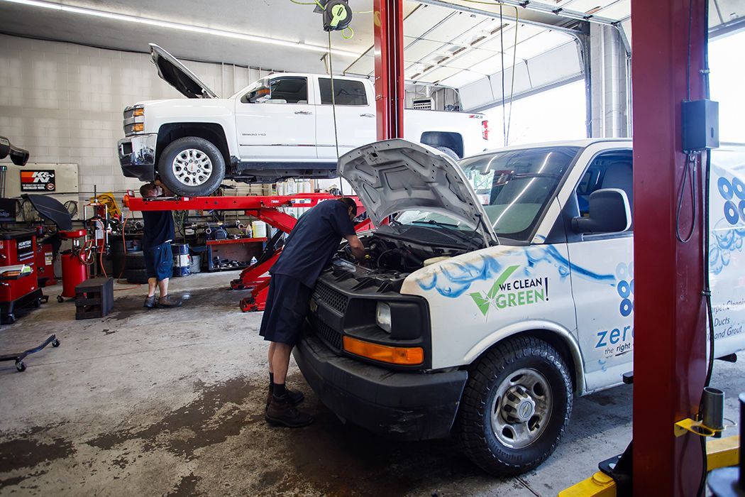 White truck lifted up in our garage as a technician focused on repairs for a fleet vehicle in our garage in Centerville, UT | Baker Automotive
